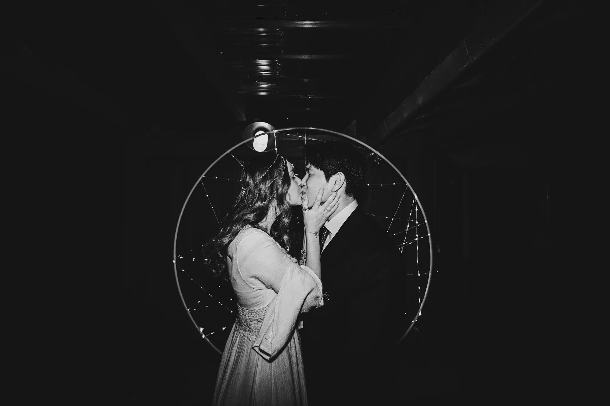 Baiser des mariés sous une arche lumineuse, en noir et blanc